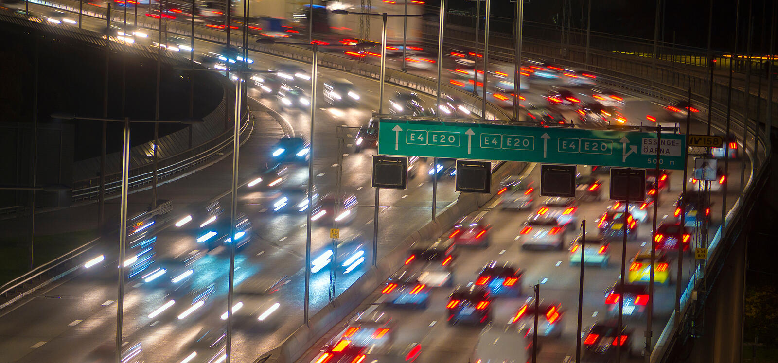 En stad vid nattid med bilar som kör på en motorväg. (AI text)