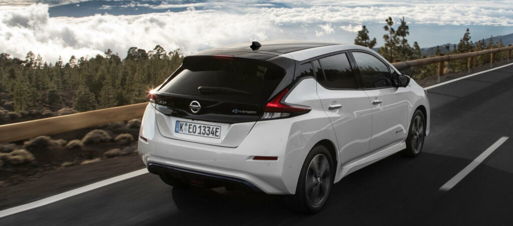 En vit Nissan Leaf kör nerför en bergsväg. (AI text)