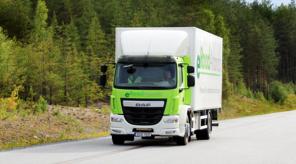 En grön lastbil kör nedför en väg. (AI text)