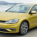 En gul Volkswagen Golf kör nerför en väg. (AI text)