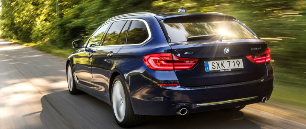 BMW X5 Touring kör nedför en landsväg. (AI text)