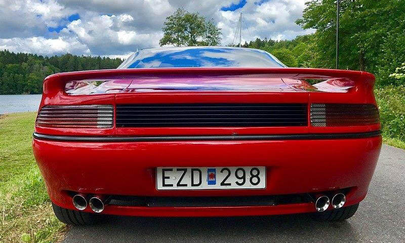 En röd sportbil parkerad vid en väg vid en sjö. (AI text)