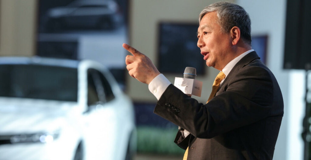 En man i kostym håller en tal på en bilmesse. (AI text)