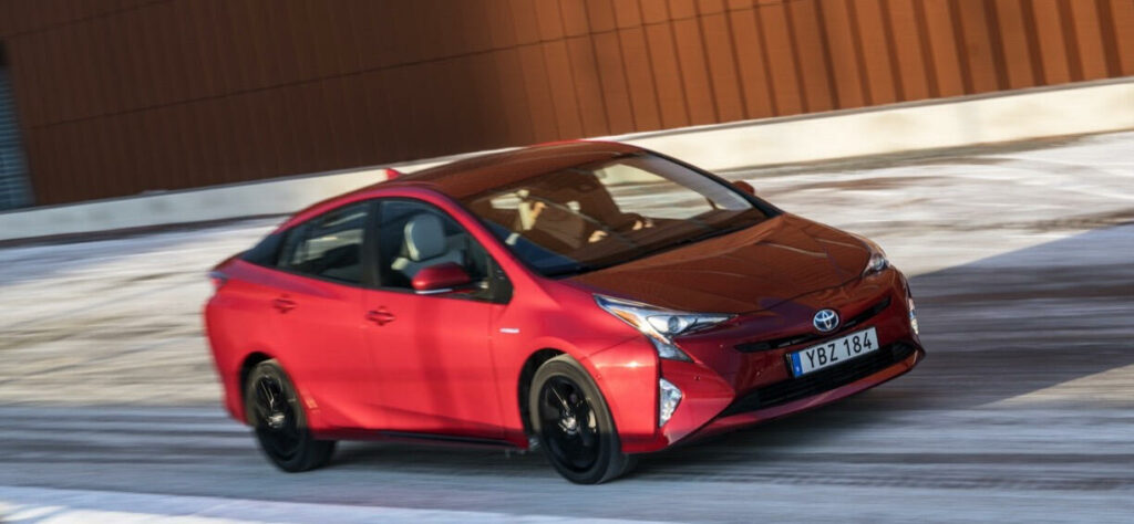 En röd Toyota Prius kör nerför en snöig väg. (AI text)