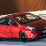 En röd Toyota Prius kör nerför en snöig väg. (AI text)