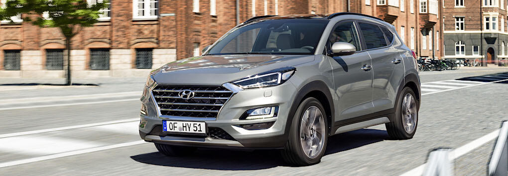 En silverfärgad SUV kör nedför en stadsgata. (AI text)