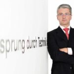 En man i kostym står bredvid en skylt. (AI text)