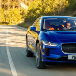 En blå jaguar i lugn takt rullar nerför en landsväg. (AI text)