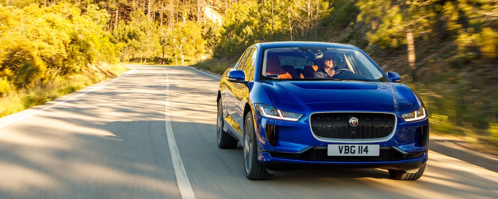 En blå jaguar i lugn takt rullar nerför en landsväg. (AI text)