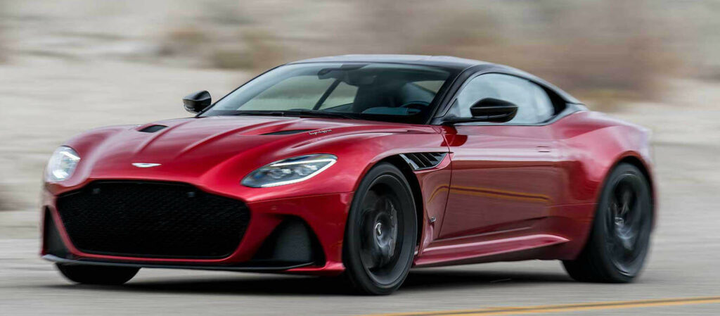 En röd Aston Martin sportbil kör längs en ökenväg. (AI text)