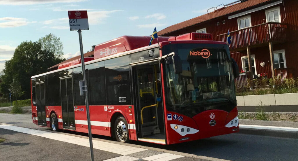 En röd buss kör nerför en gata. (AI text)