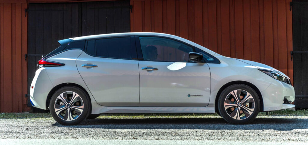En vit Nissan Leaf parkerad framför en lada. (AI text)