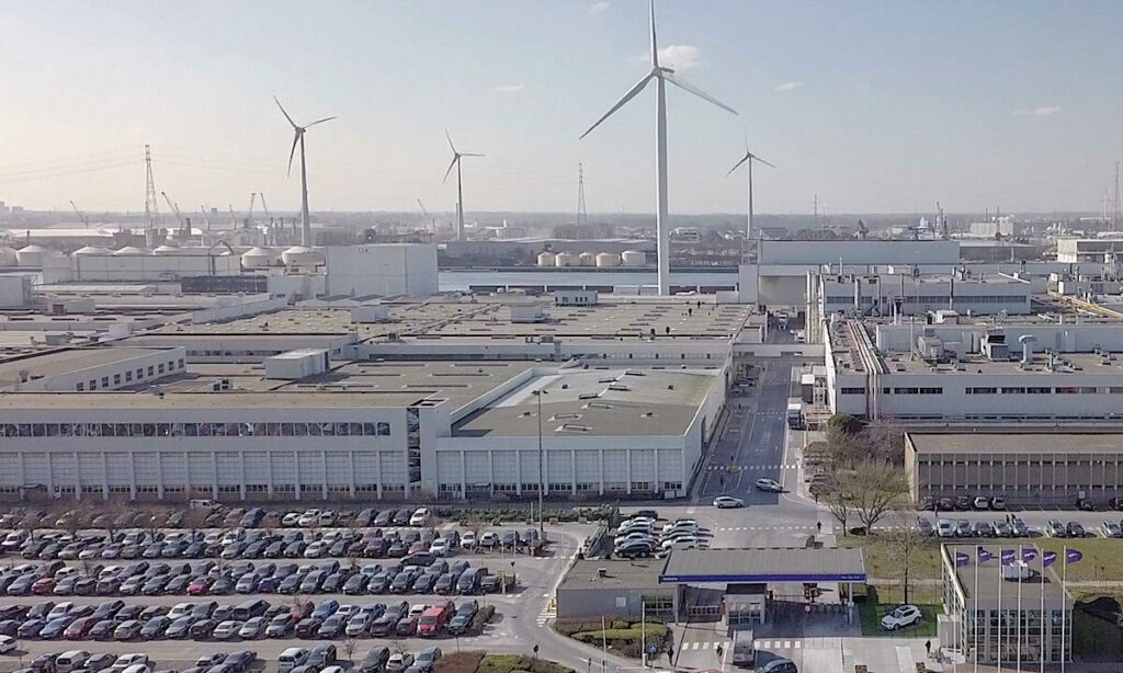 En fabrik med vindkraftverk i bakgrunden (AI text)