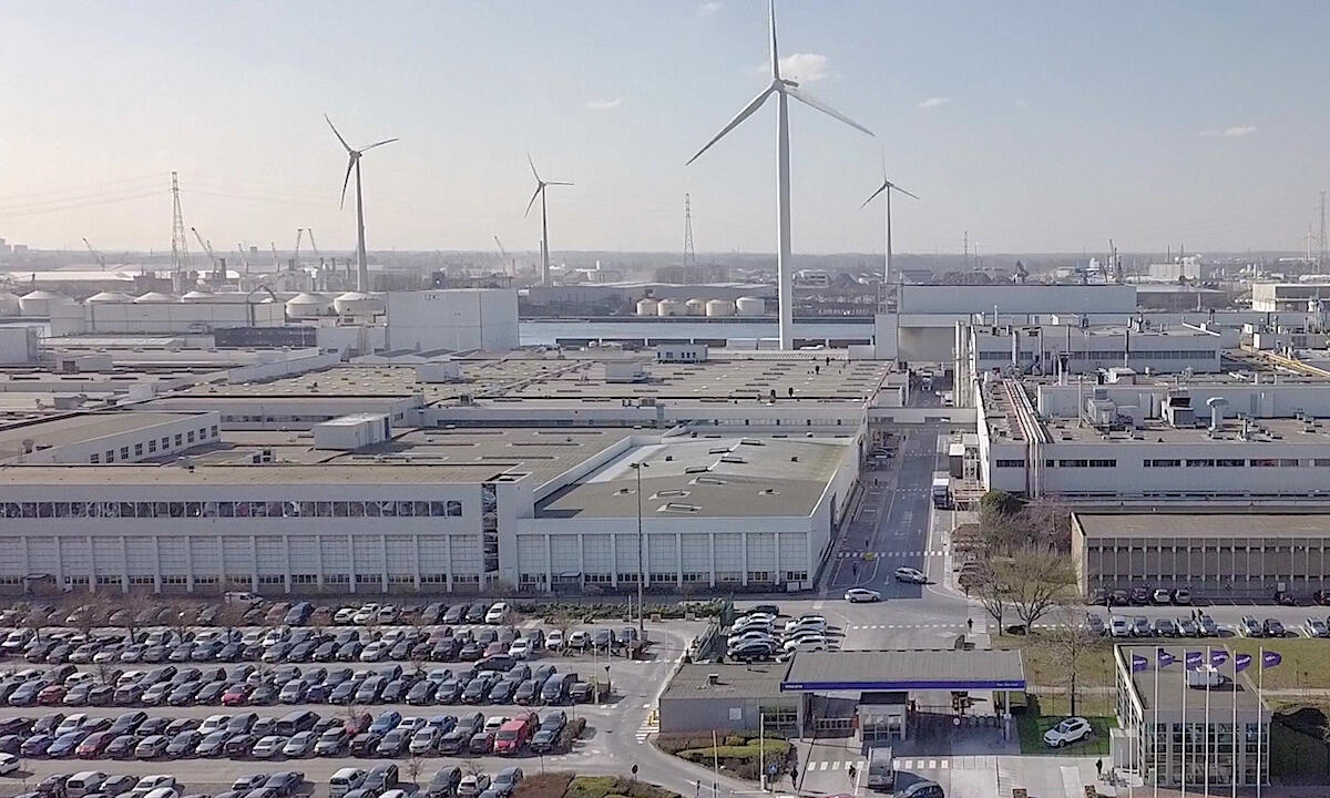 En fabrik med vindkraftverk i bakgrunden (AI text)