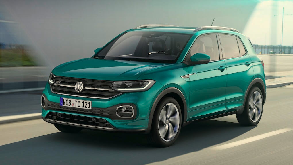 En grön Volkswagen T-Cross-terrängbil kör längs en stadsgata. (AI text)
