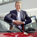 En man i kostym står bredvid en röd bil. (AI text)