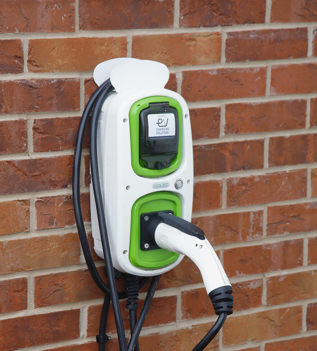 En grön elbil laddar på en mur av gula tegelstenar. (AI text)