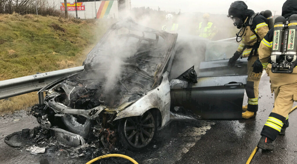 Brandmän släckar bilbrand på gatan. (AI text)