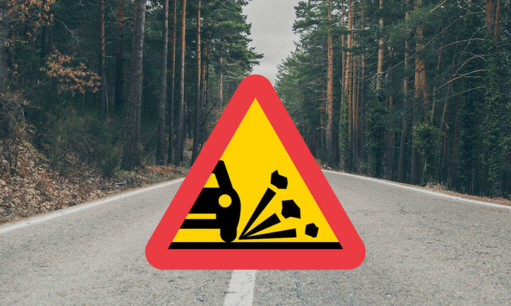 En bil kör nerför en väg med en varningsskylt. (AI text)