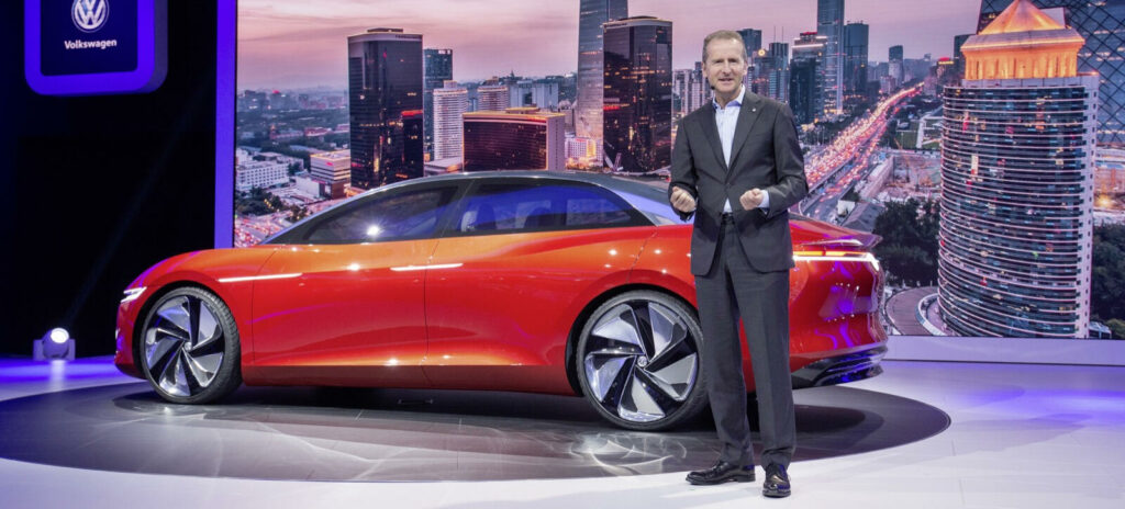 En man i kostym står bredvid en röd Volkswagen ID. (AI text)