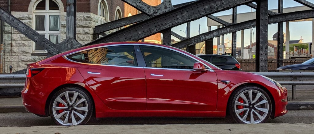 Tesla Model 3 parkerad framför en bro (AI text)