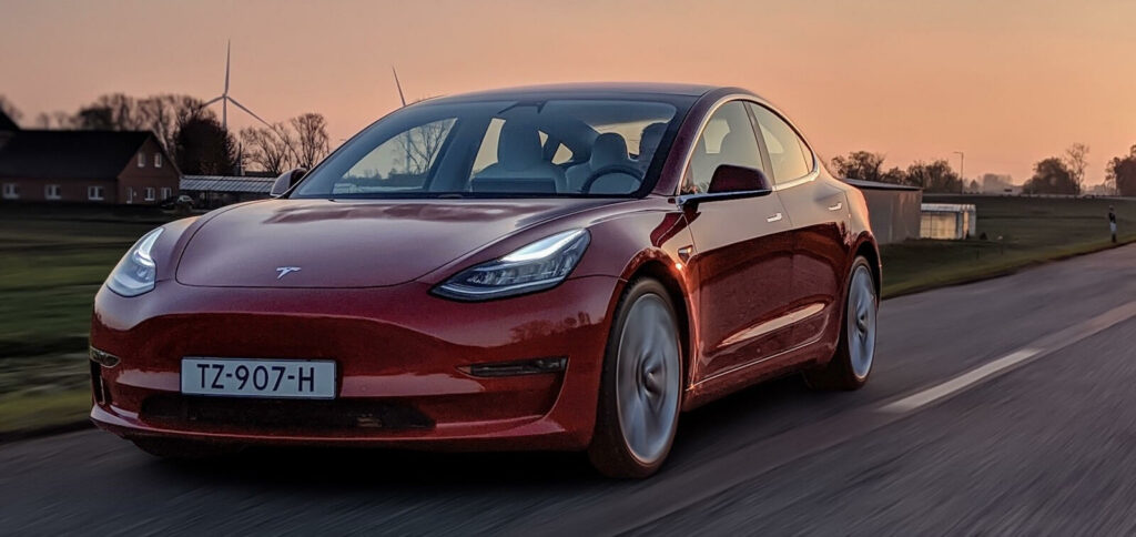 En Tesla Model 3 kör nerför en landsväg. (AI text)