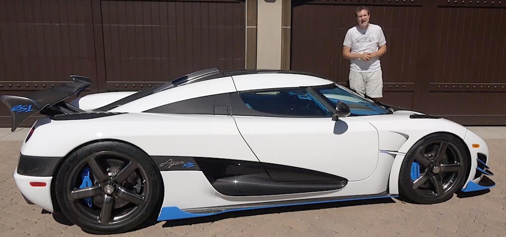 En man står bredvid en vit och blå sportbil. (AI text)