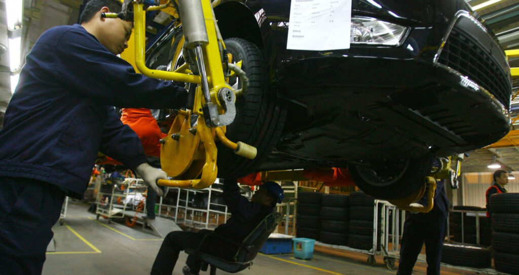 En arbetare arbetar på en bil på en fabrik. (Foto: Reuters) (AI text)