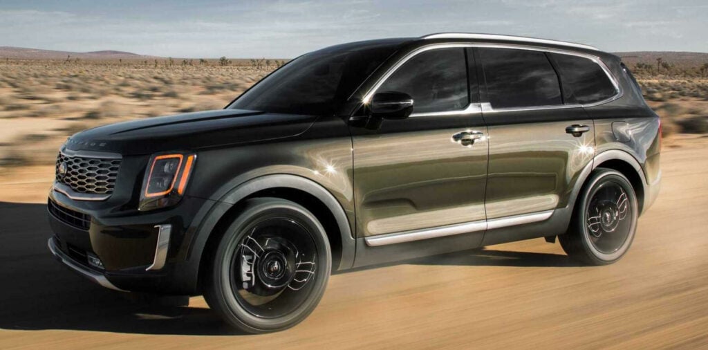 En svart och gröngul Kia Telluride kör längs en ökenväg. (AI text)