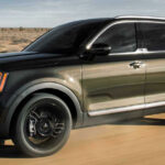 En svart och gröngul Kia Telluride kör längs en ökenväg. (AI text)