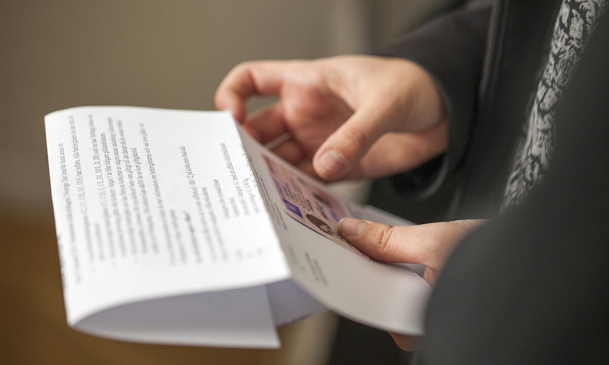 En person håller ett papper framför en bil. (AI text)