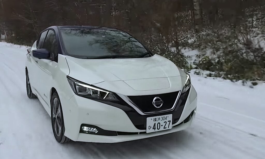 En vit Nissan Leaf kör nedför en snöig väg. (AI text)