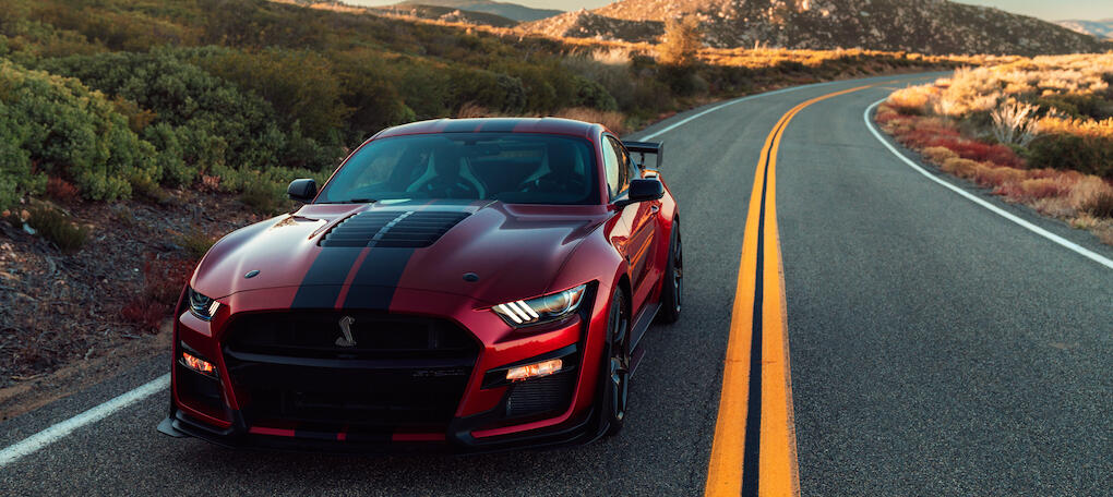 En röd Ford Mustang GT kör nedför en bergsväg. (AI text)