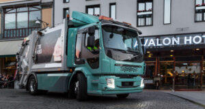 En grön Volvo-lastbil kör nerför en stadsgata. (AI text)