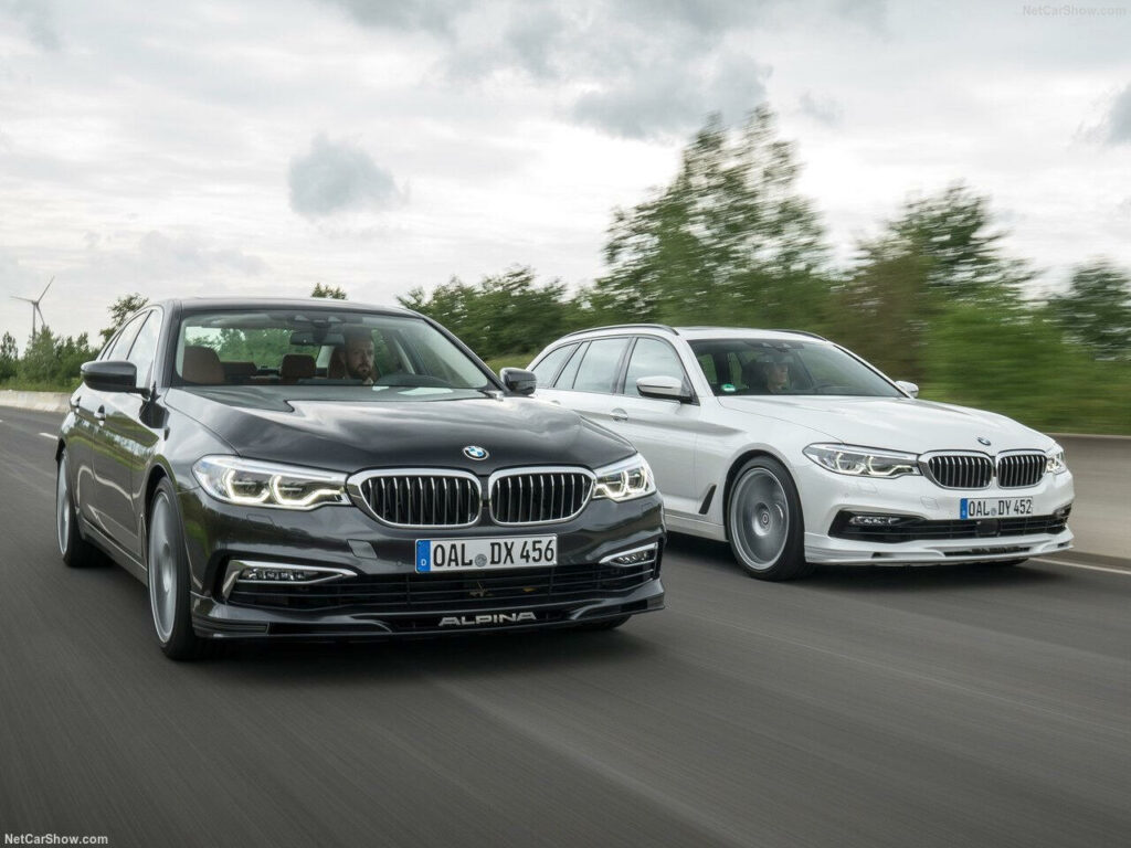 Två BMW 5-serie-sedaner kör längs en landsväg. (AI text)