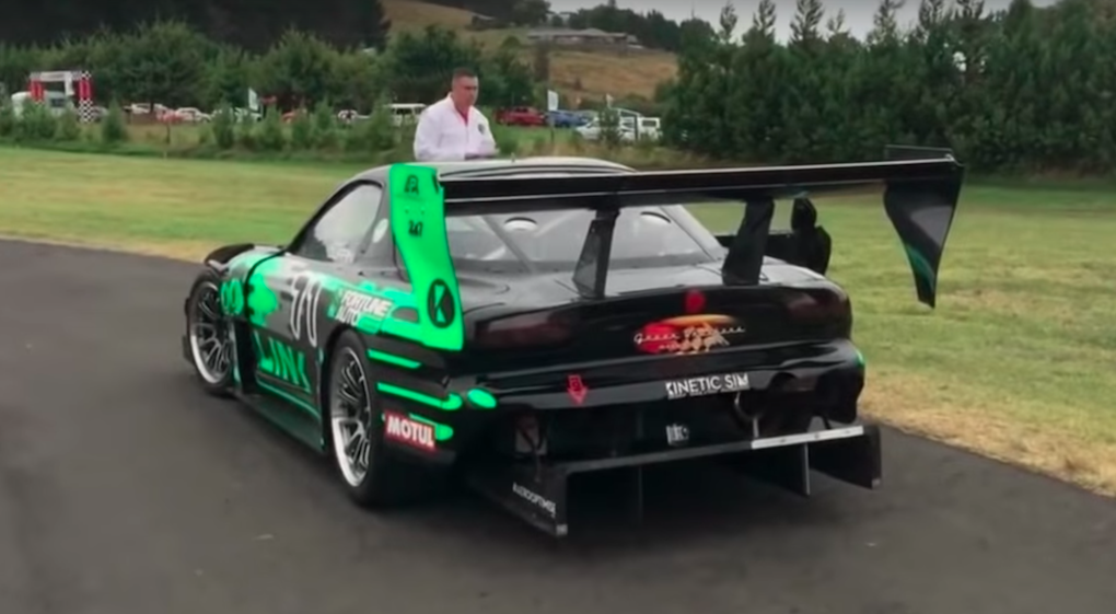 En grön och svart racerbil parkerad på en gräsmattad backe. (AI text)