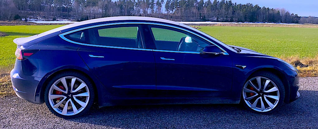 Tesla Model 3 parkerad på en grusväg i en åker. (AI text)