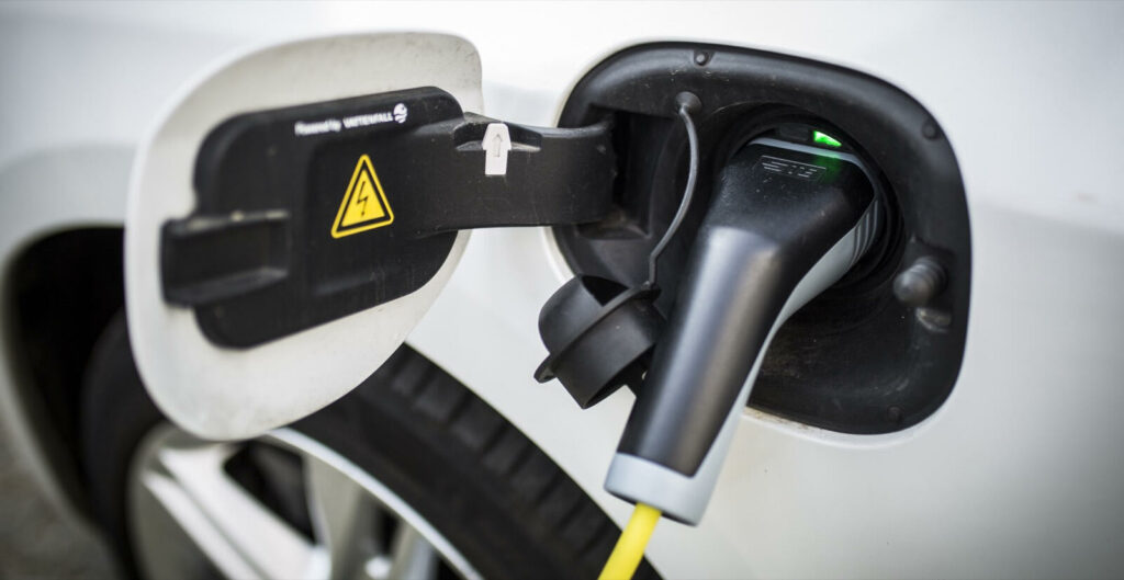 En vit bil är uppkopplad till en elbilsladdare. (AI text)