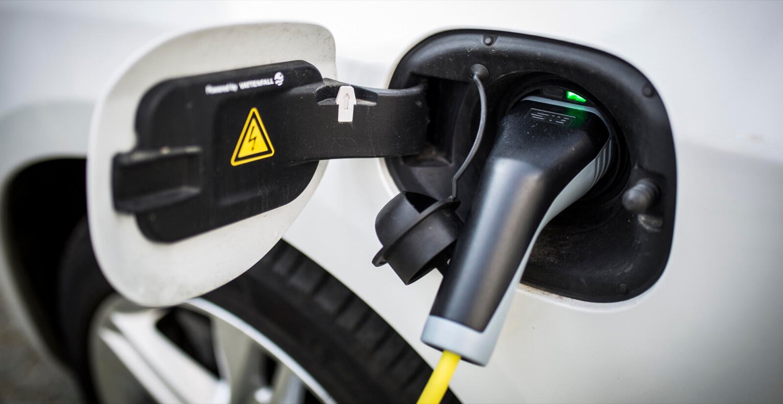 En vit bil är uppkopplad till en elbilsladdare. (AI text)