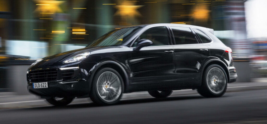 En svart Porsche Cayenne kör längs en stadsgata. (AI text)