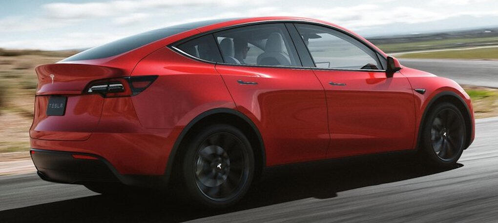 En röd Tesla Model Y kör nerför en väg. (AI text)