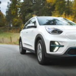 En vit Kia Soul kör nerför en landsväg. (AI text)