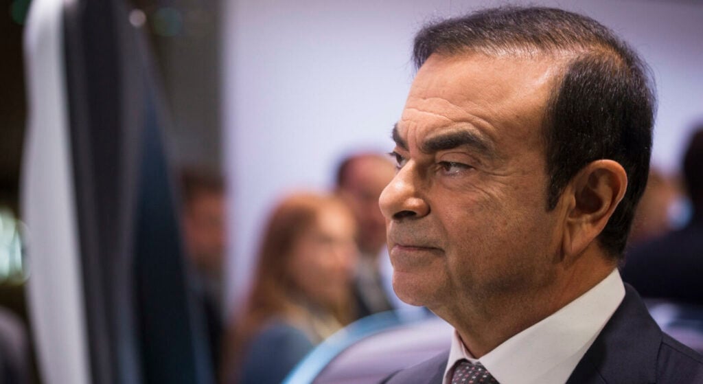 En man i kostym och slips står framför en bil. (AI text)