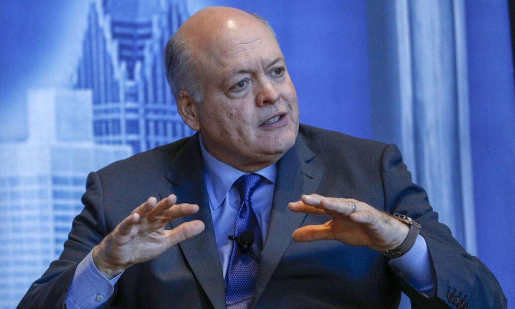 En man i kostym och slips talar till en kamera. (AI text)