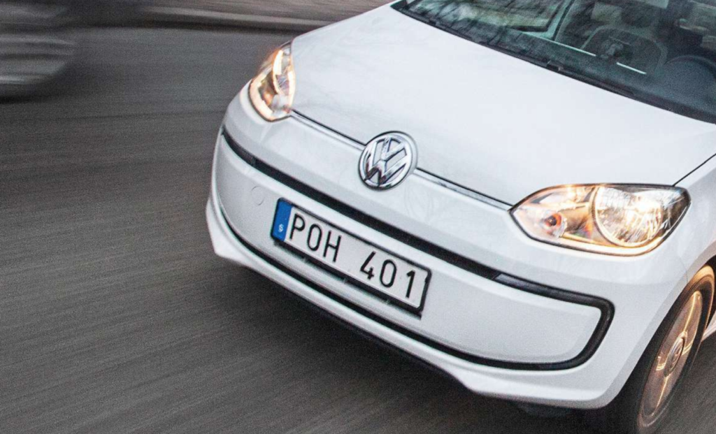 En vit Volkswagen up! kör ner gatan. (AI text)