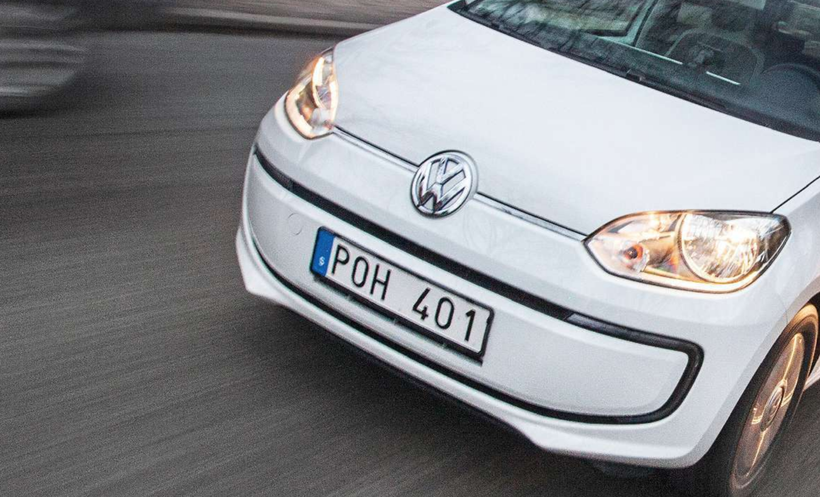 En vit Volkswagen up! kör ner gatan. (AI text)