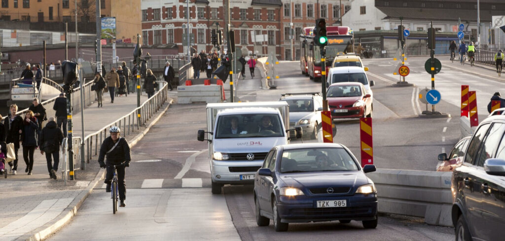 En stadsgata med bilar och folk. (AI text)