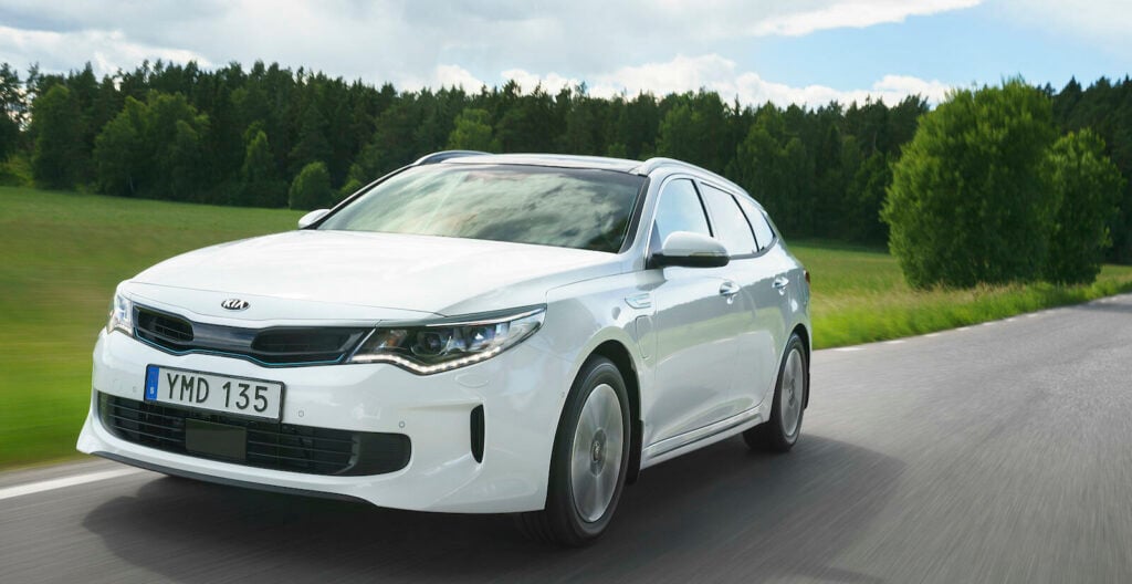 En vit Kia Optima kör nedför en landsväg. (AI text)