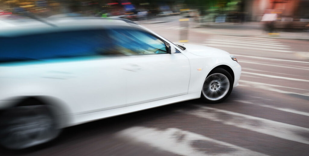 En vit bil kör nedför en stadsgata. (AI text)