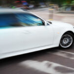 En vit bil kör nedför en stadsgata. (AI text)